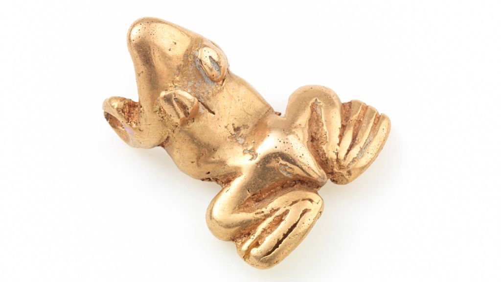 Ein goldener Frosch in einer liegenden Position auf weissem Hintergrund strahlt im Licht.