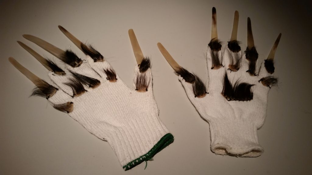 Auf dem Foto sind zwei weisse Handschuhe aus Bali zu sehen, an deren Fingern lange Krallen befestigt sind