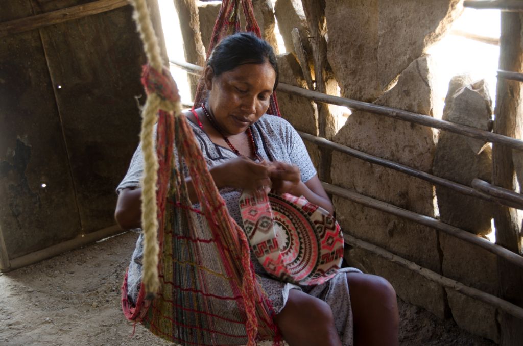 Auf einer bunten Hängematte sitzend arbeitet eine Frau namens Eleida konzentriert an einer Tasche. 