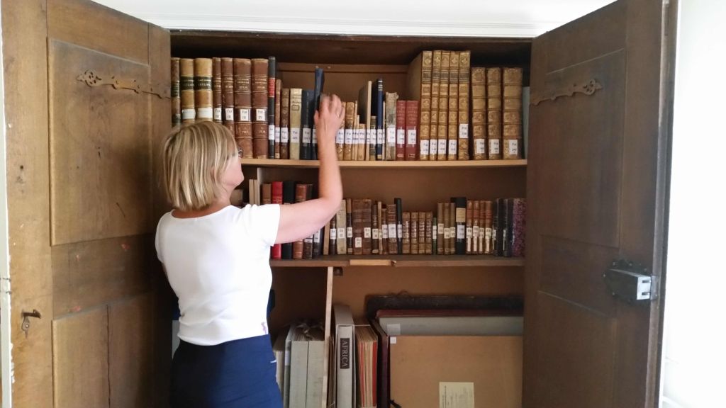 Die Bibliothekarin Angelika Kutter steht vor einem geöffneten alten Schrank, in dem sich auf vier Gestellen teils sehr alte Bücher befinden.