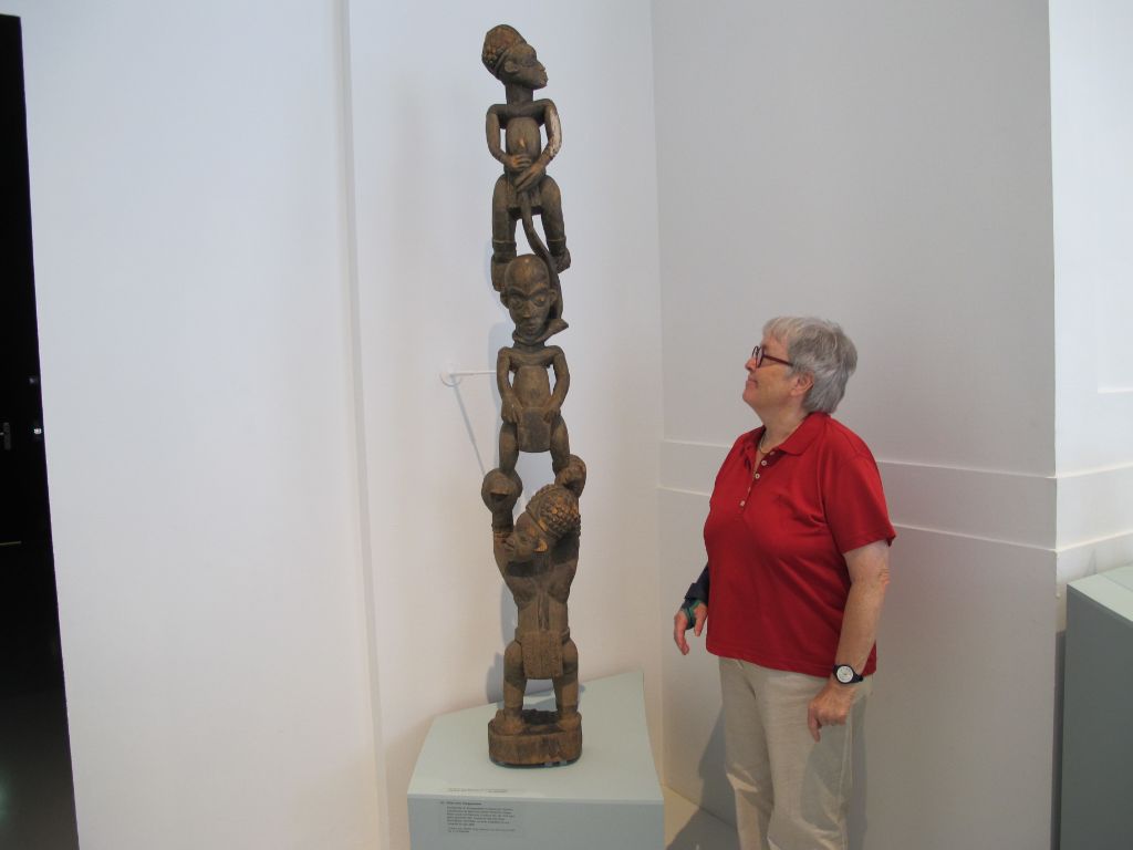 Frau Zierath steht neben dem Objekt, welches sie um mindestens drei Köpfe überragt. Die Holzskulptur zeigt eine Erhängungsszene, in welcher zwei Männer, einer unten, einer oben, einen anderen aufzuhängen versuchen.