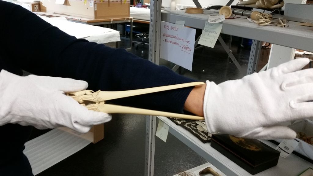 Auf dem Foto zeigt Frau Geissmann, die weisse Handschuhe trägt, wie ein Handstuhstrecker aus Elfenbein verwendet wird