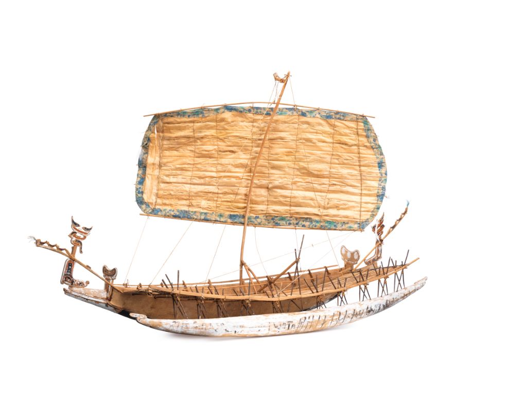 Das Foto zeigt ein Modellboot mit grossem Segel. Vorne und hinten im Boot stehen kleine Figuren, die das Boot zu lenken scheinen.