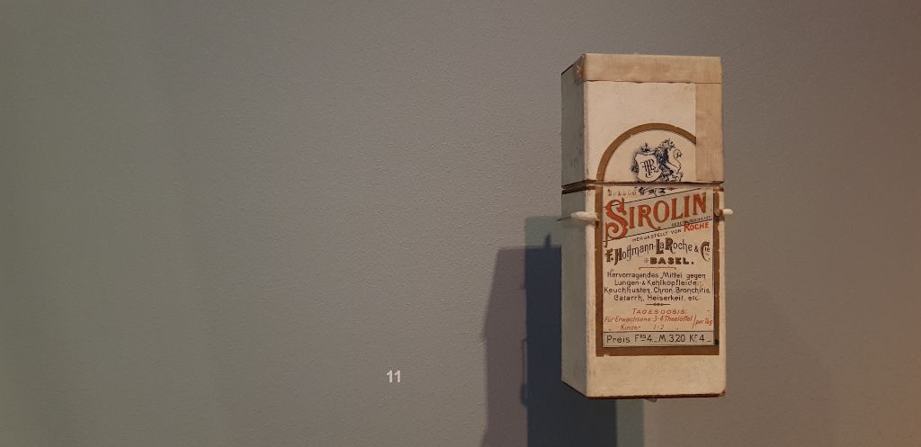Im Museum ist eine Verpackung des Medikaments Sirolin ausgestellt. Diese ist etwa handgross, der weisse Karton ist vergilbt.