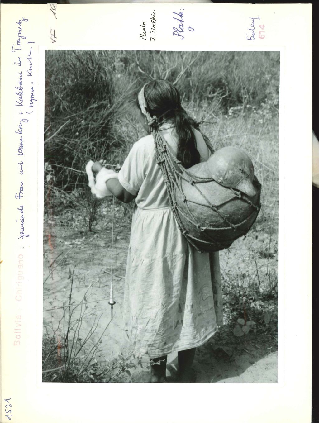 Eine lateinamerikanische Frau trägt mit einem Tragnetz eine schwere Last und spinnt dabei einen Faden.