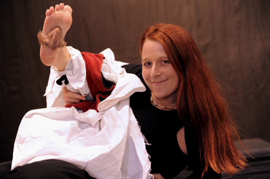 Das Foto zeigt Anne Klinge wie sie in die Kamera schaut, ein Fuss streckt sich hoch, Bein und Fuss stellen einen Kellner dar