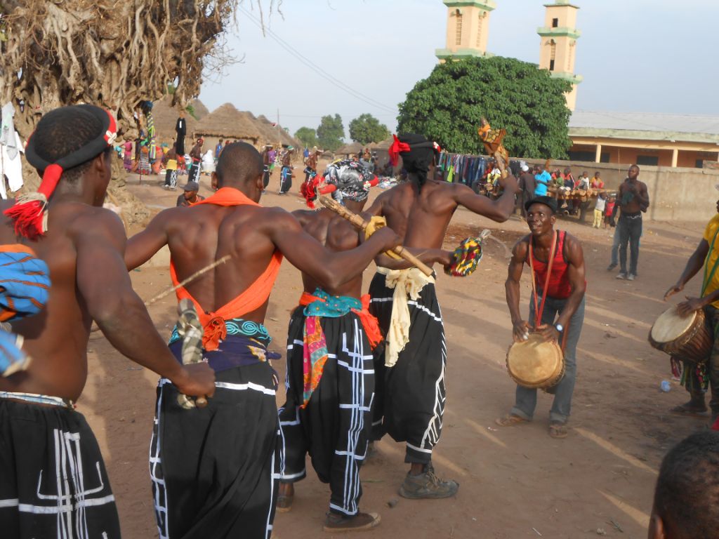 Das Bild zeigt tanzende und trommelnde Musiker auf einem Platz, wo Zuschauer das Ganze verfolgen