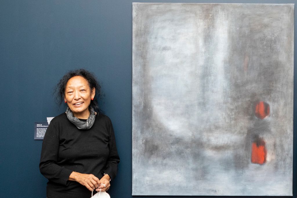 Künstlerin in schwarzem Pullover steht neben einem Gemälde von ihr