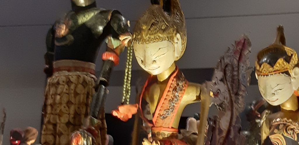 Das Foto zeigt Stabfiguren. In der Mitte steht Arjuna, prächtig gekleidet von Kopf bis Fuss. Er hat sehr feine Gesichtszüge.