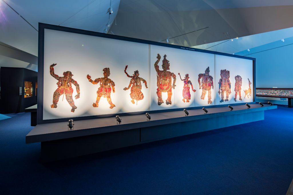 Das Foto zeigt eine grosse Leinwand, auf der mannshohe Schattenfiguren aufgenäht sind. Es sind neun Figuren, die von hinten angeleuchtet werden.