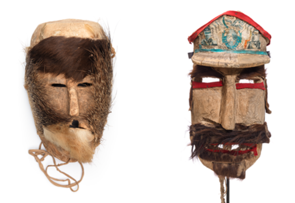 Das Foto zeigt zwei Masken aus Holz und Haaren, bei denen die Augen nur Schlitze sind, beide tragen Bärte resp. Schnäuze, die rechte Maske zudem einen Hut