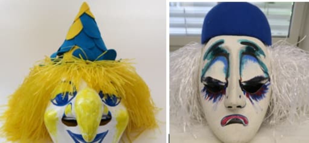 Zwei Masken: links blau-gelb-weisses Gesicht mit gelbem Strohhaar und einer Plätzlizipfelmütze, rechts eine Ueli-Maske mit halbgeschlossenen Augen, weissem Haar und blauer Kappe