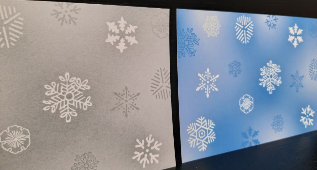 Zwei Karten in Postkartengrösse stehen nebeneinander, eine blau-weiss, eine grau-weiss, beide zeigen verschiedene Schneeflockenmotive