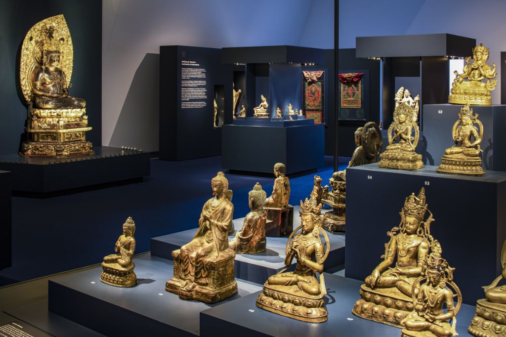 Blick in eine Vitrine mit blauen Podesten auf denen viele goldene Buddhafiguren thronen