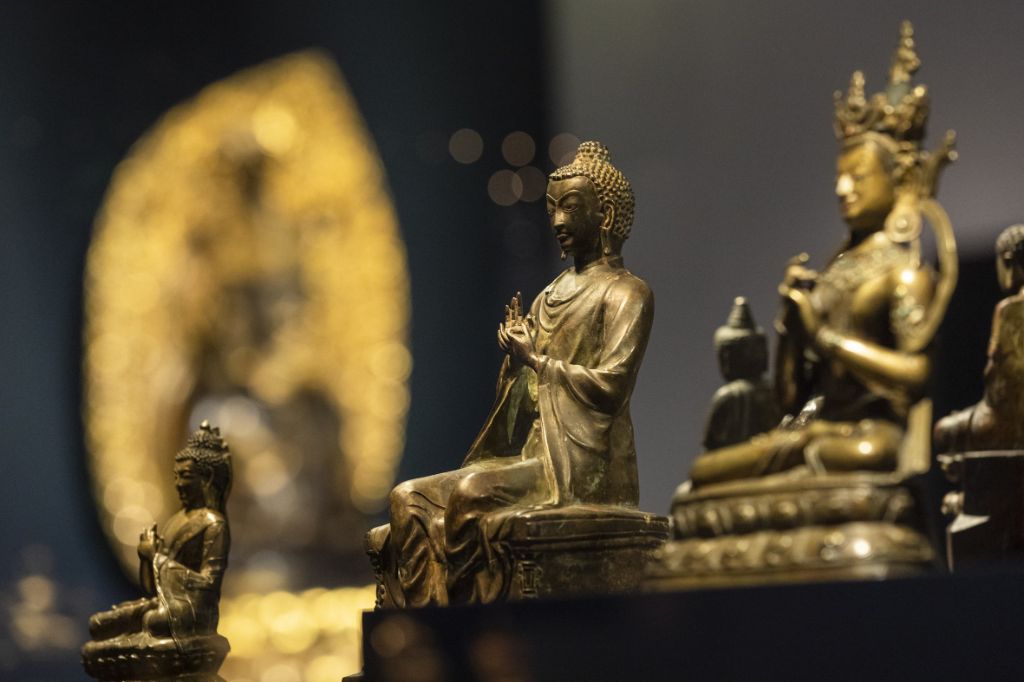 Drei Buddhafiguren im Vordergrund, golden, links und rechts im Schneidersitz, der in der Mitte lässt die Beine baumeln