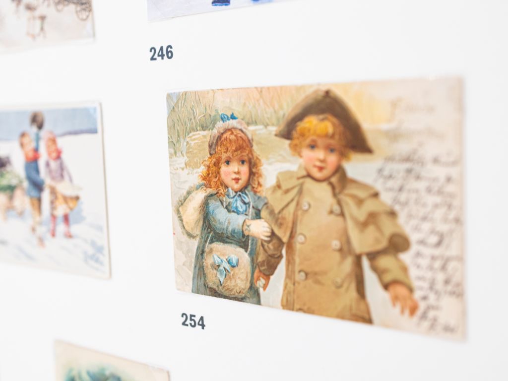 Fünf Karten auf weissem Grund, von denen nur eine deutlich zu erkennen ist. Sie zeigt ein Mädchen und einen Knaben und daneben handgeschriebenen Text.