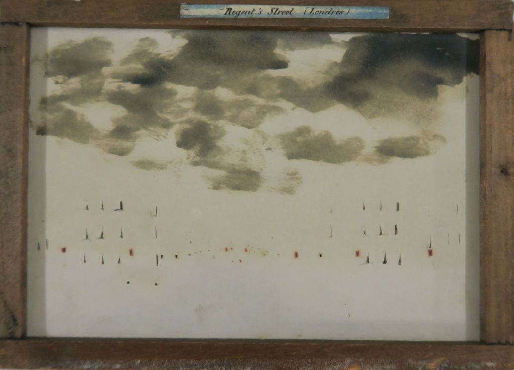 Rückseite eines Bildes in einem Holzrahmen: Man sieht oben schwarze Wolken und darunter ganz kleine Dreiecke auf weissem Hintergrund.