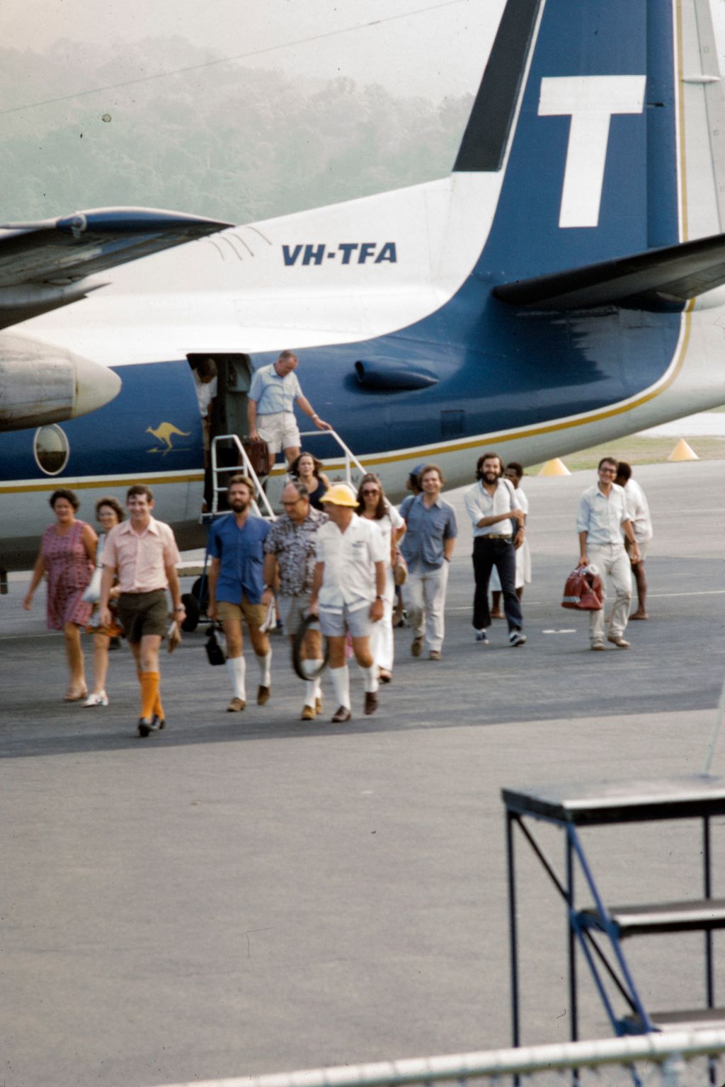 Rumpf eines Flugzeuges mit einem grossen weissen T auf der Heckflosse. Aus dem Flugzeug steigen Menschen und laufen übers Rollfeld.