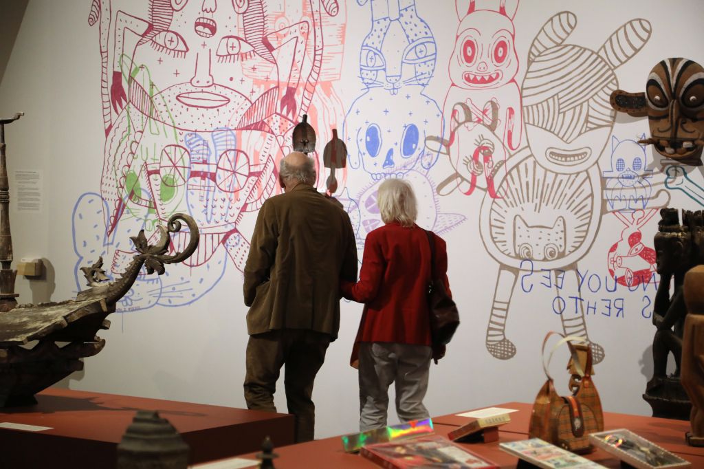  Zwei Personen betrachten bunte Wandkunst in einem Museum mit ausgestellten Artefakten