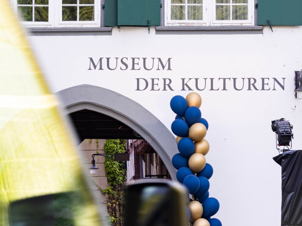 Ein Eingang mit dem Schriftzug "Museum der Kulturen", dekoriert mit blauen und goldenen Luftballons