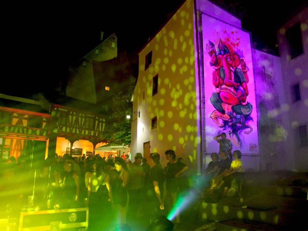 Museumshof bei Nacht mit tanzenden jungen Leuten, mit Lichtpunkten angestrahlte Fassade