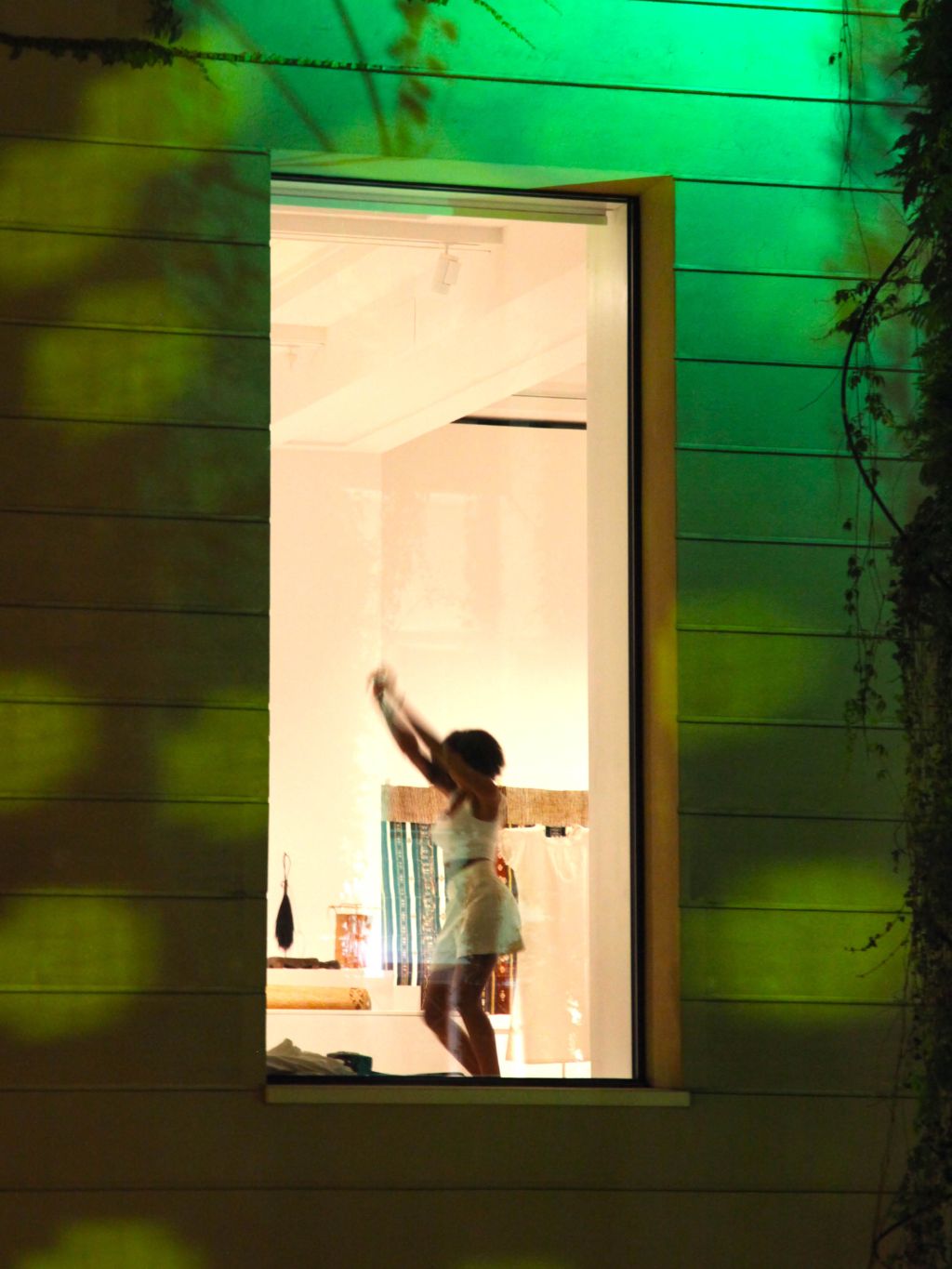 Museumsfassade bei Nacht mit hellerleuchtenden Fenster. Im Fenster tanzt eine Frau mit kurzem weissen Kleid.