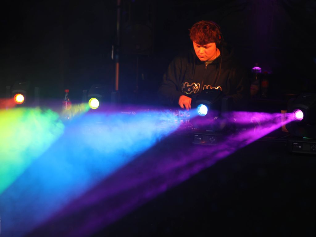 Ein DJ konzentriert sich auf seine Musik mit buntem Licht und Rauch um ihn herum auf der Bühne