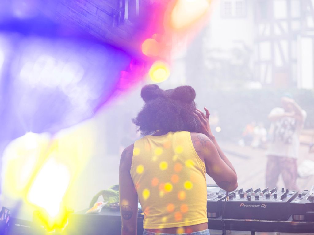 Ein DJ in einem gelben Top mixt Musik auf einem Open-Air-Festival mit flirrenden Lichtern