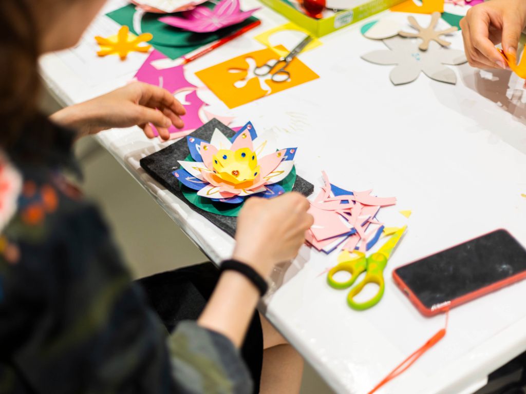 Basteltisch mit  aus farbigen Papier. Links im Bild Umrisse einer Frau, die an der Lotosblüte arbeitet.