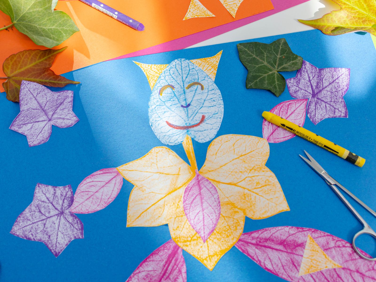 Fantasiewesen aus Blättern, dahinter farbiges Papier, Schere und Stifte