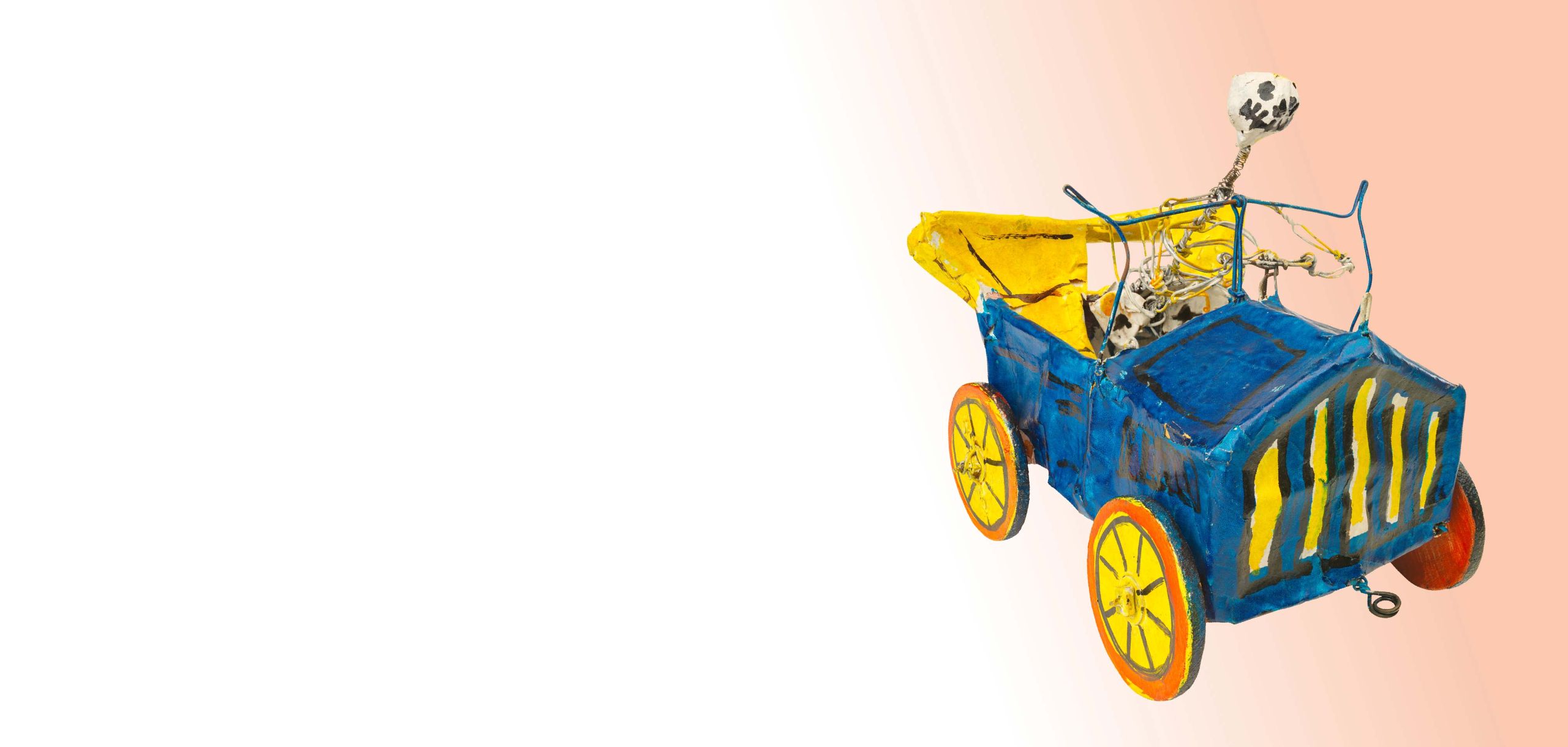 Mexikanische Totenfigur aus Pappmache, in Form eines Skeletts, welches ein blaues Oldtimer-Auto mit offenem gelben Verdeck, roten Rädern mit gelben Felgen steuert.