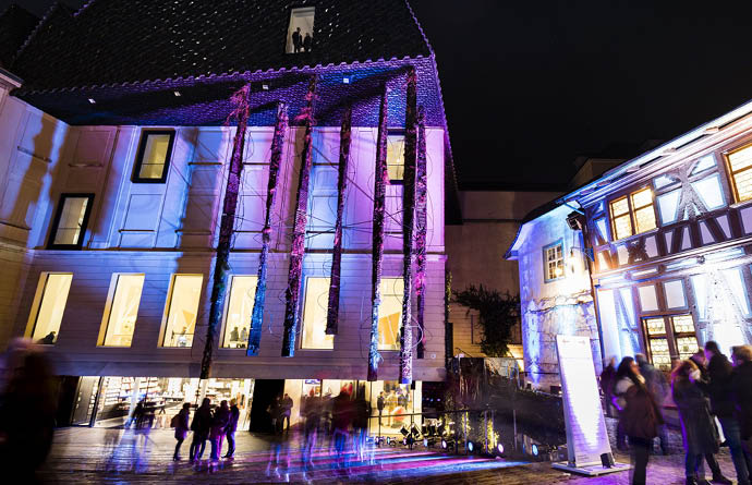Ein dunkler Hof wird bei Nacht von bunten Lichtern beleuchtet, während Menschen vorbei schlendern