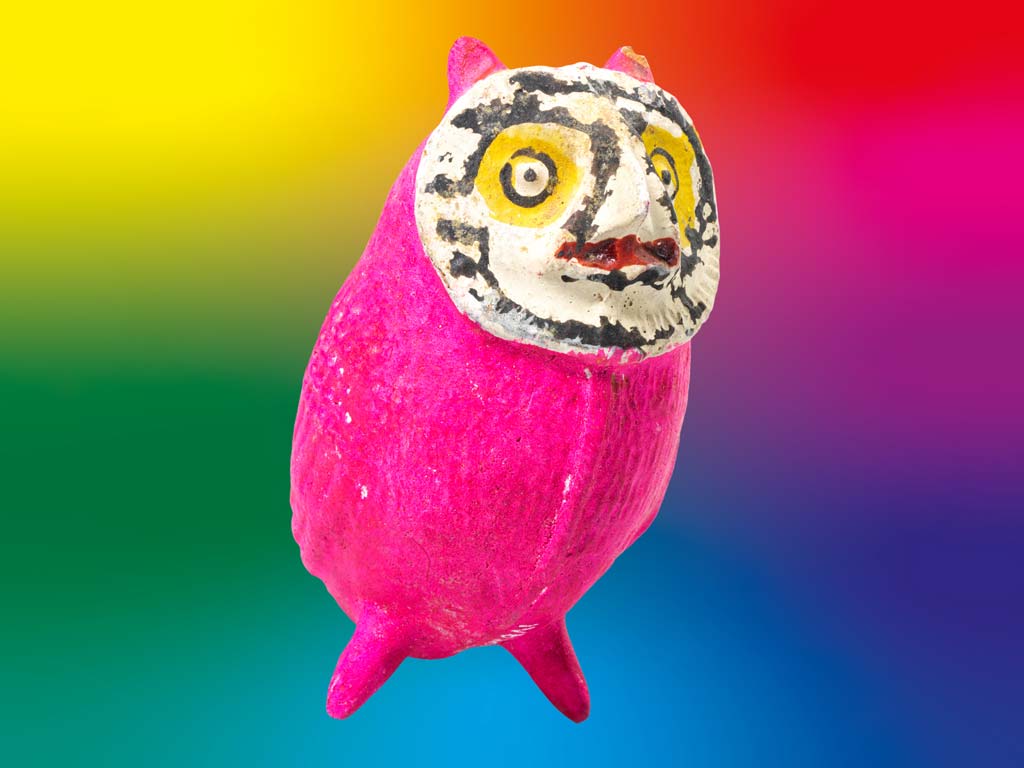 Figurine de hibou rose avec visage blanc et yeux bordés de jaune sur fond arc-en-ciel éclatant